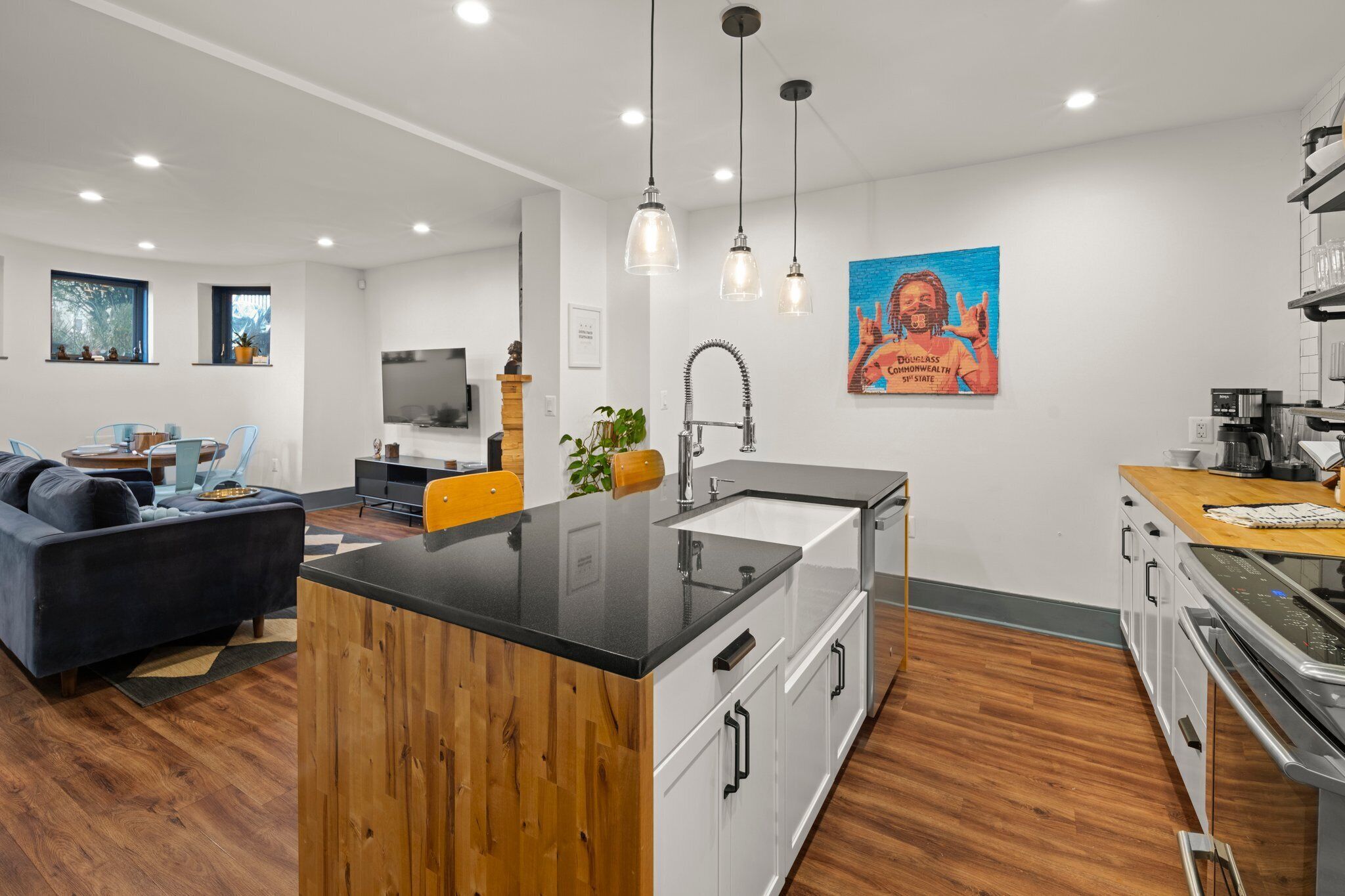 A modern kitchen with a central island, white cabinetry, and a wooden countertop. There is a dining area with a blue sofa and a coffee machine on the counter.