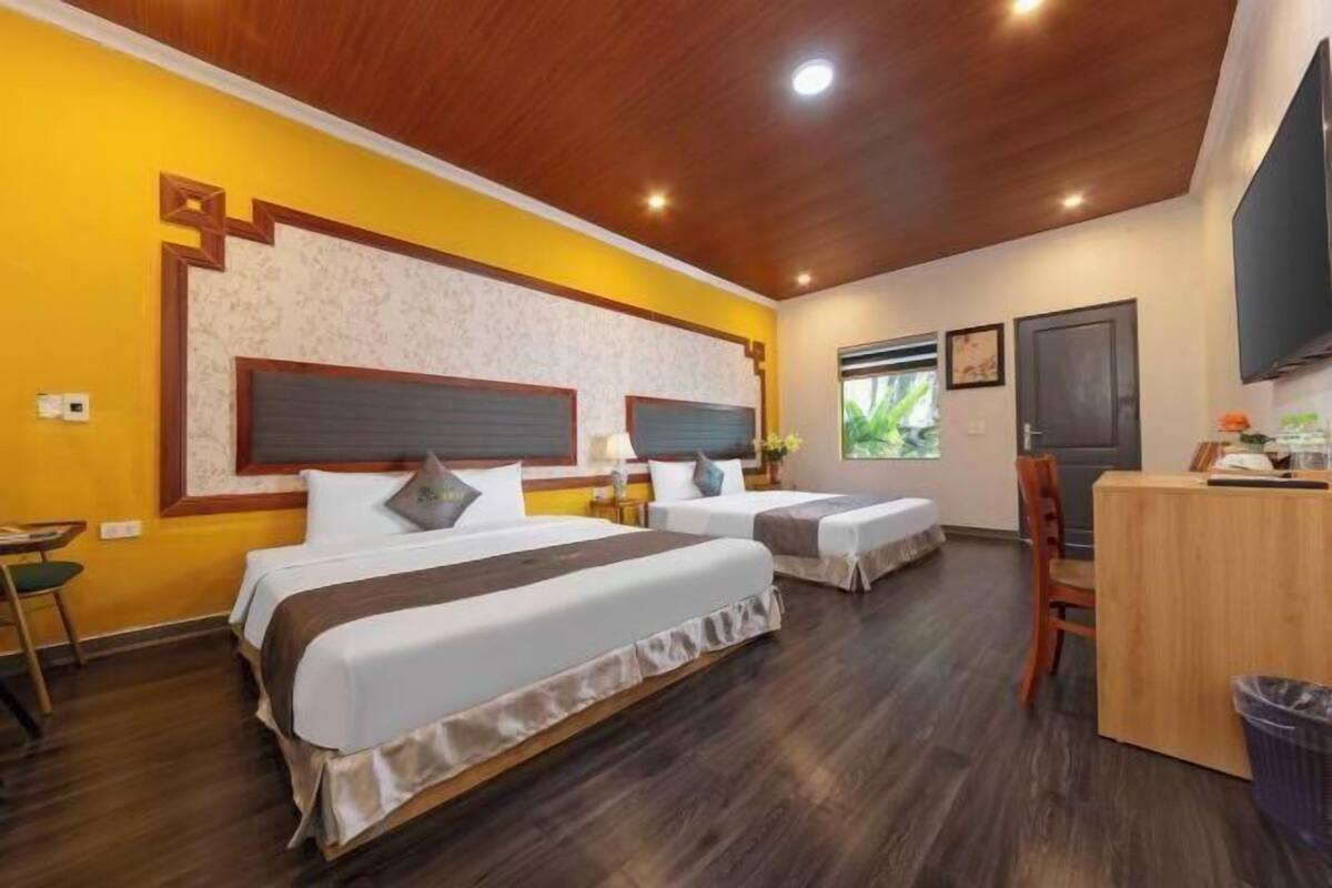 A hotel room with two beds, a desk, a chair, and a TV.