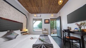 A hotel room with a bed, bedside table, lamp, TV, and a view of the outdoors. - Trang An Ecorest Resort & Spa (Hoa Lu District)