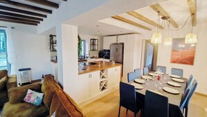Un amplio espacio de estar con techo de madera, una mesa de comedor preparada para seis personas y una cocina al fondo.