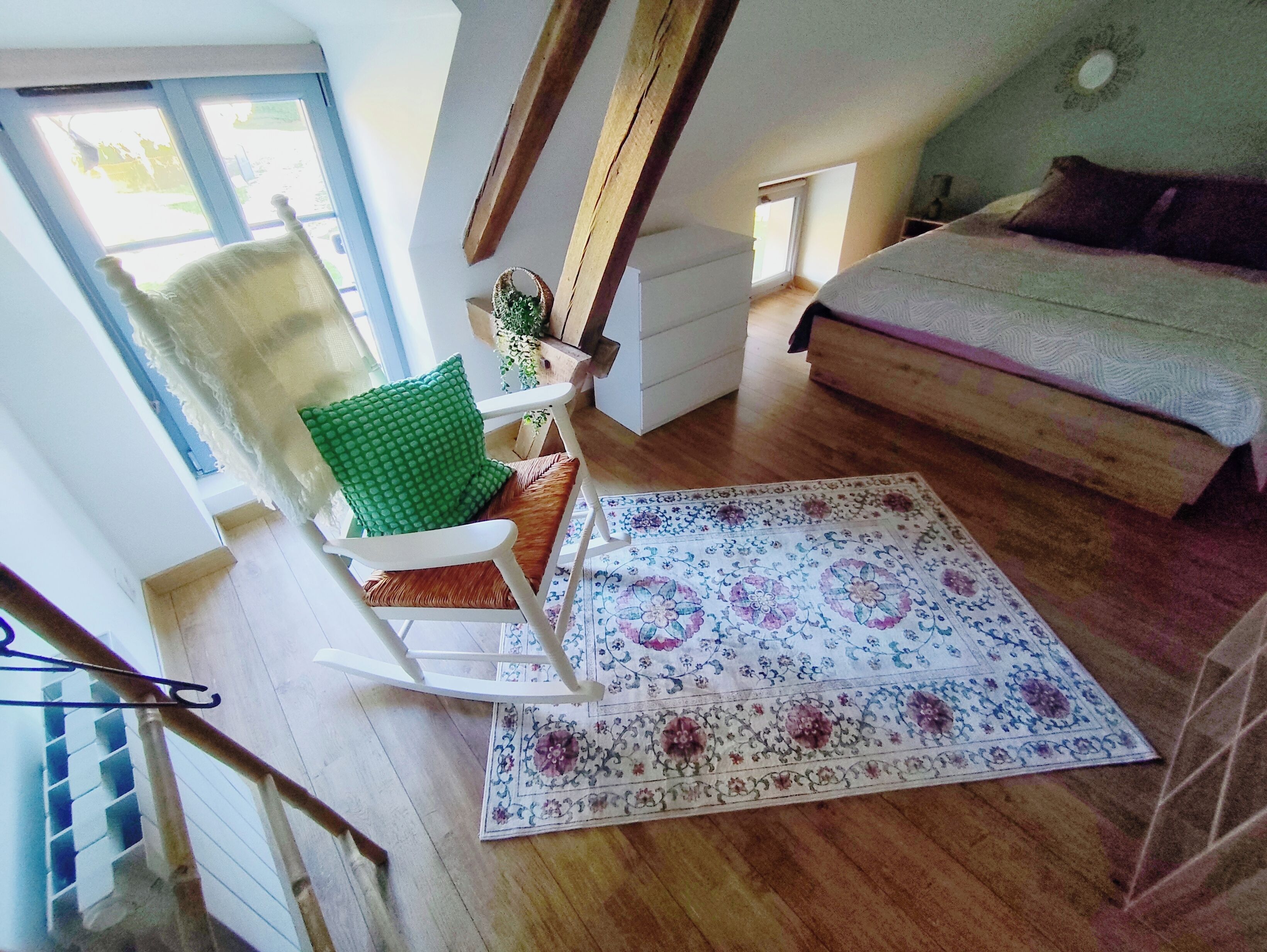 Een kamer met een houten vloer, een groene fauteuil, een witte bank, een kamerbreed tapijt met een patroon, en een trap.