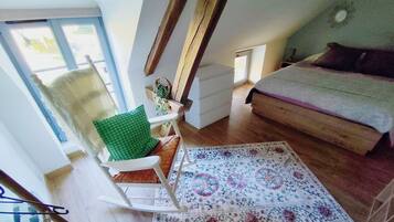 Een kamer met een houten vloer, een groene fauteuil, een witte bank, een kamerbreed tapijt met een patroon, en een trap.