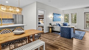 Een moderne woonkamer met een houten eettafel, blauwe fauteuils met een patroon, een blauwe bank en een groot raam met uitzicht op bomen.