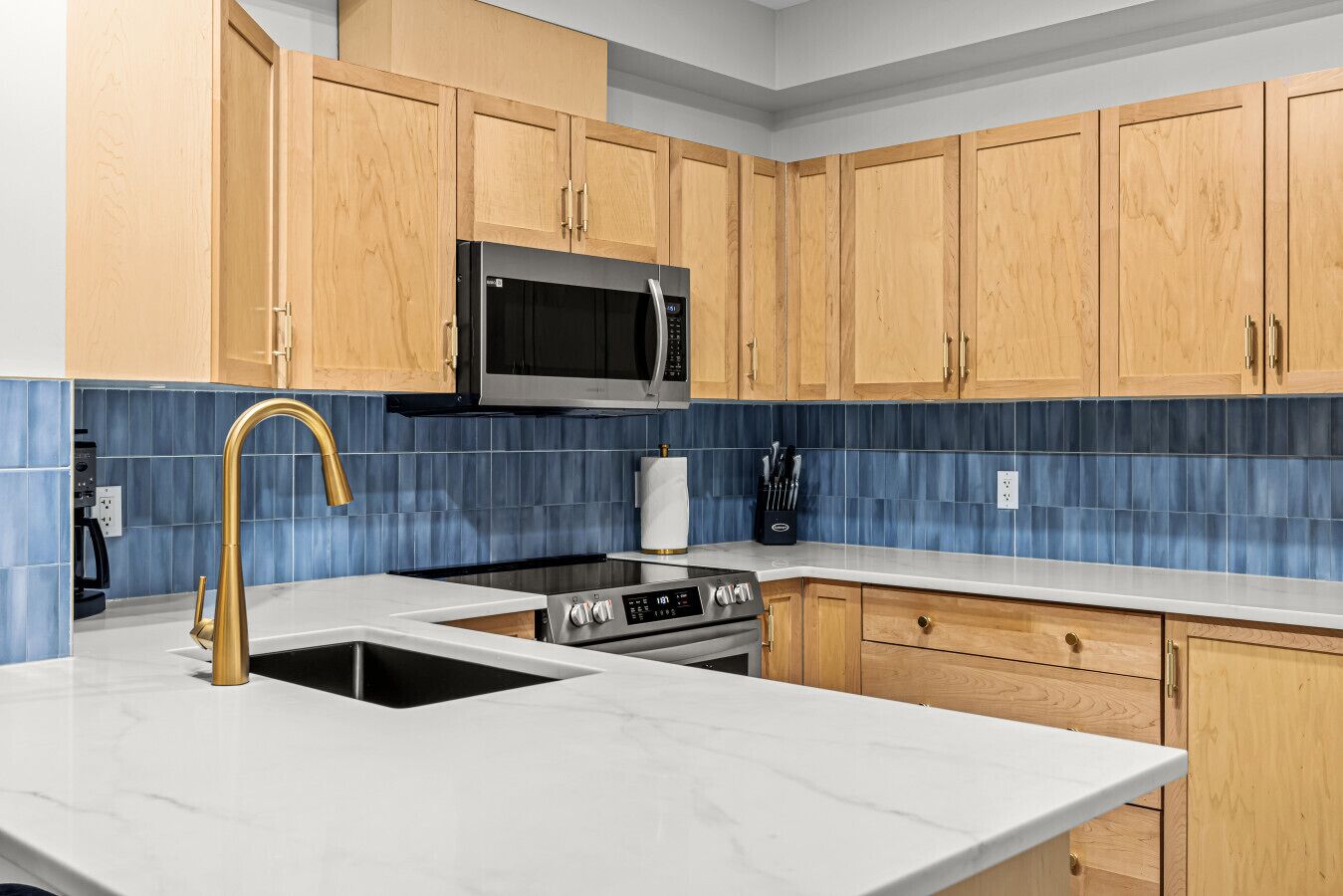 A modern kitchen with wooden cabinets, a stainless steel microwave, a gas stove, and a marble countertop.