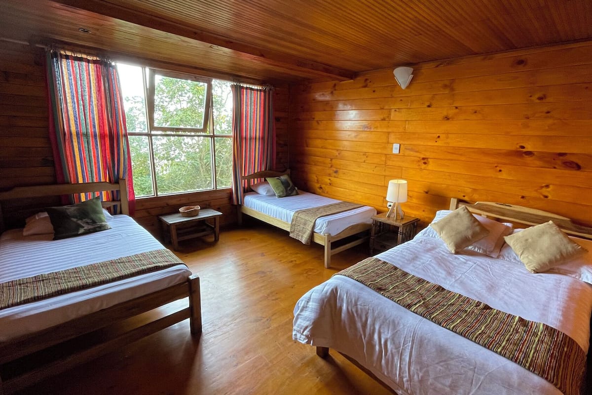 A cabin with three wooden beds, a small table, and a lamp.