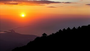 Un atardecer sobre un paisaje montañoso con construcciones tradicionales de techo de paja silueteadas contra el cielo.
