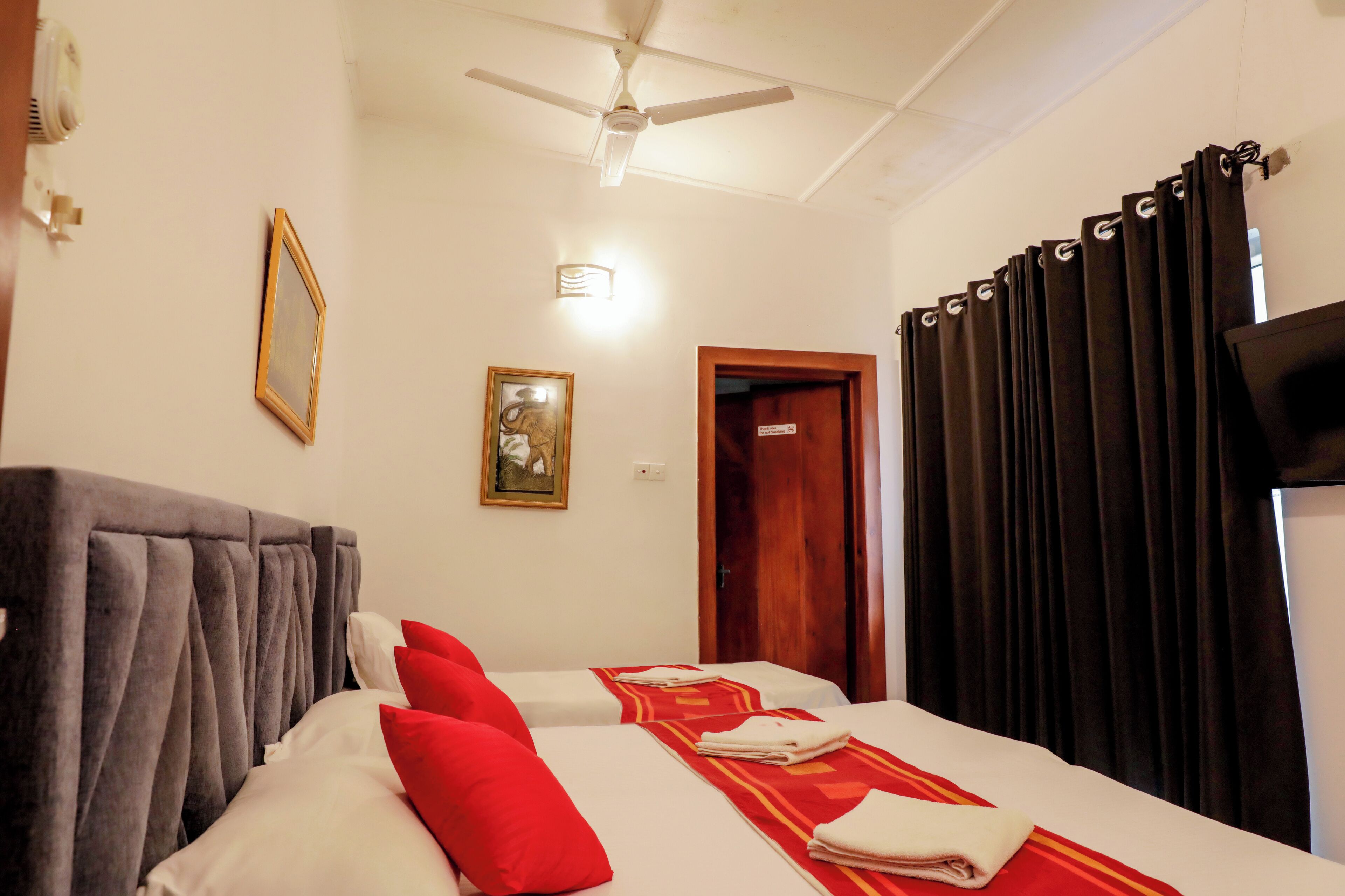 Una habitación de hotel con una cama, un ventilador de techo, un cuadro enmarcado y una puerta.