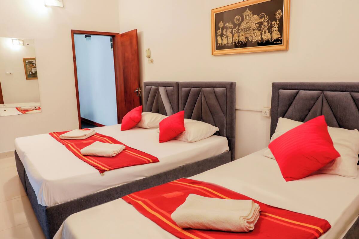 A hotel room with two beds, each with a grey headboard, red and white pillows, and a red and white striped blanket.