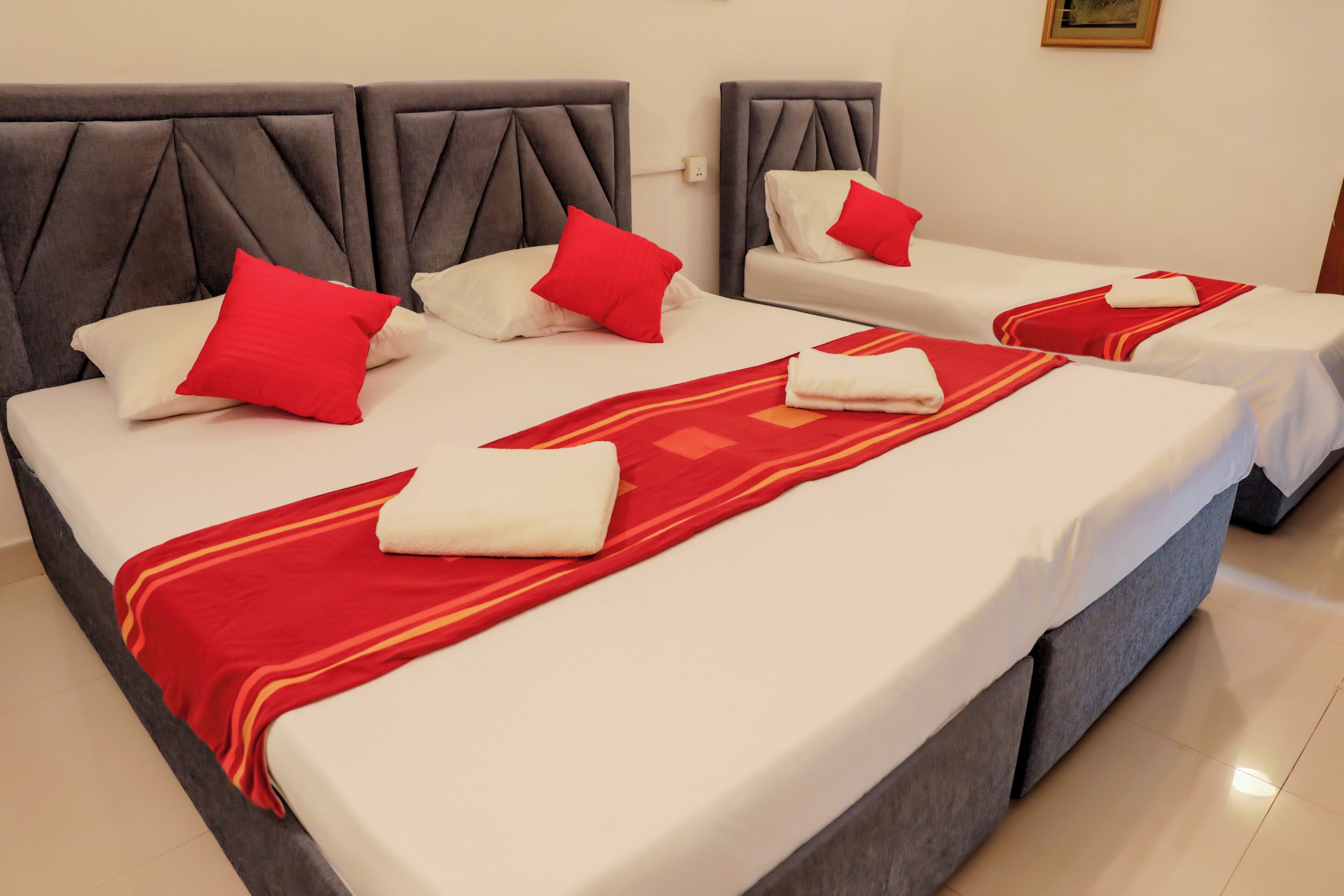 Une chambre d’hôtel avec deux lits, chacun doté d’une tête de lit rembourrée de couleur grise, de draps blancs et d’éléments décoratifs rouges.