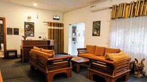 A cozy living room with wooden furniture, a television, and a glass door leading to a bathroom. - Cozy Nest Kandy Villa (Kandy)