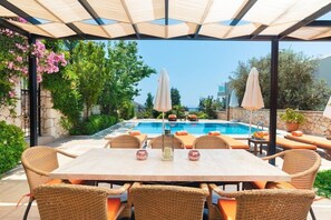 A poolside area with a table and chairs, umbrellas, and a view of the pool and greenery. - Secluded Villa with Large Private Pool & Beautiful Gardens | Walk to Kalkan Town (Kalkan)