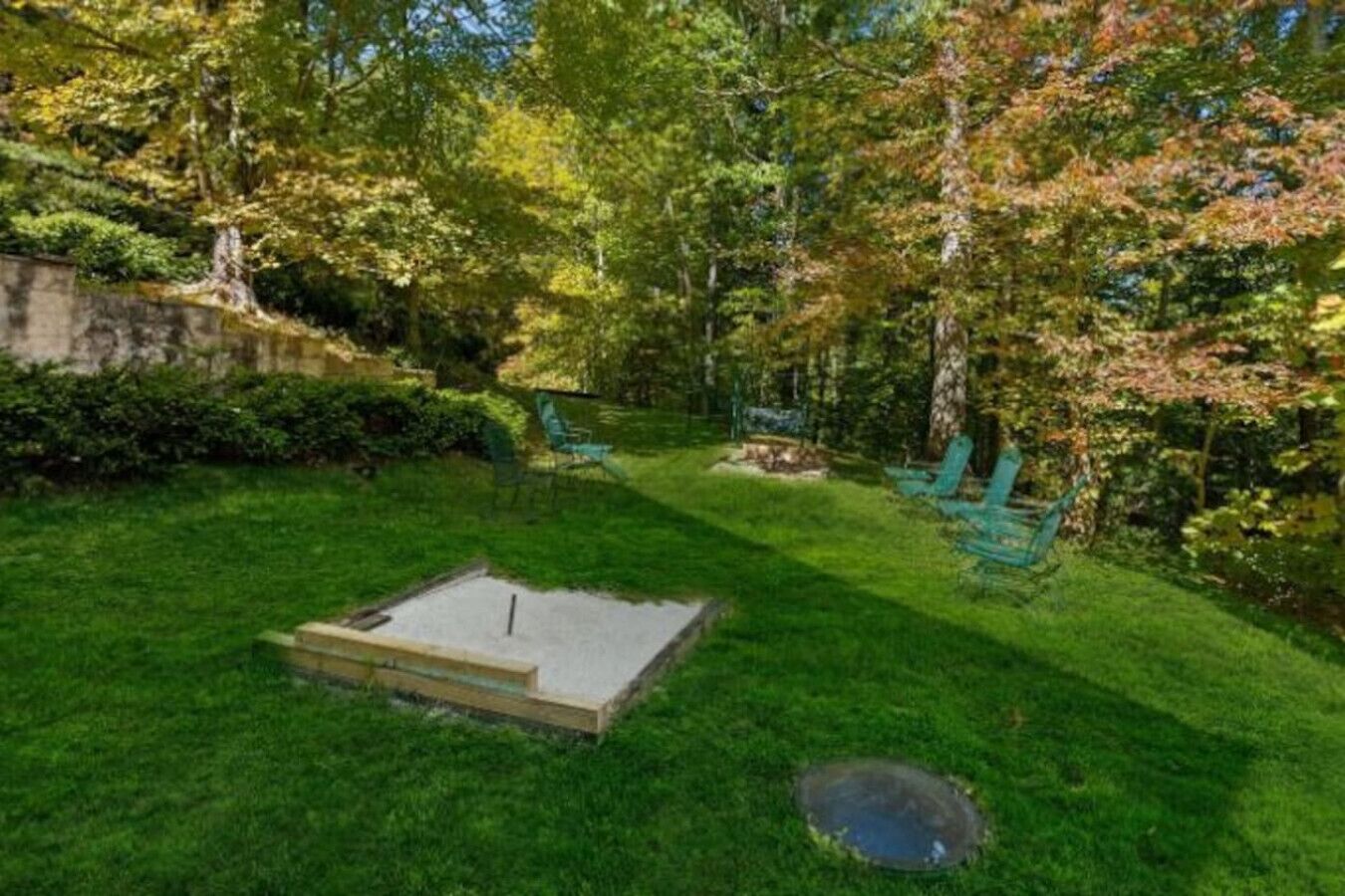 A well-maintained garden with a small pond, a concrete play area, and green chairs.