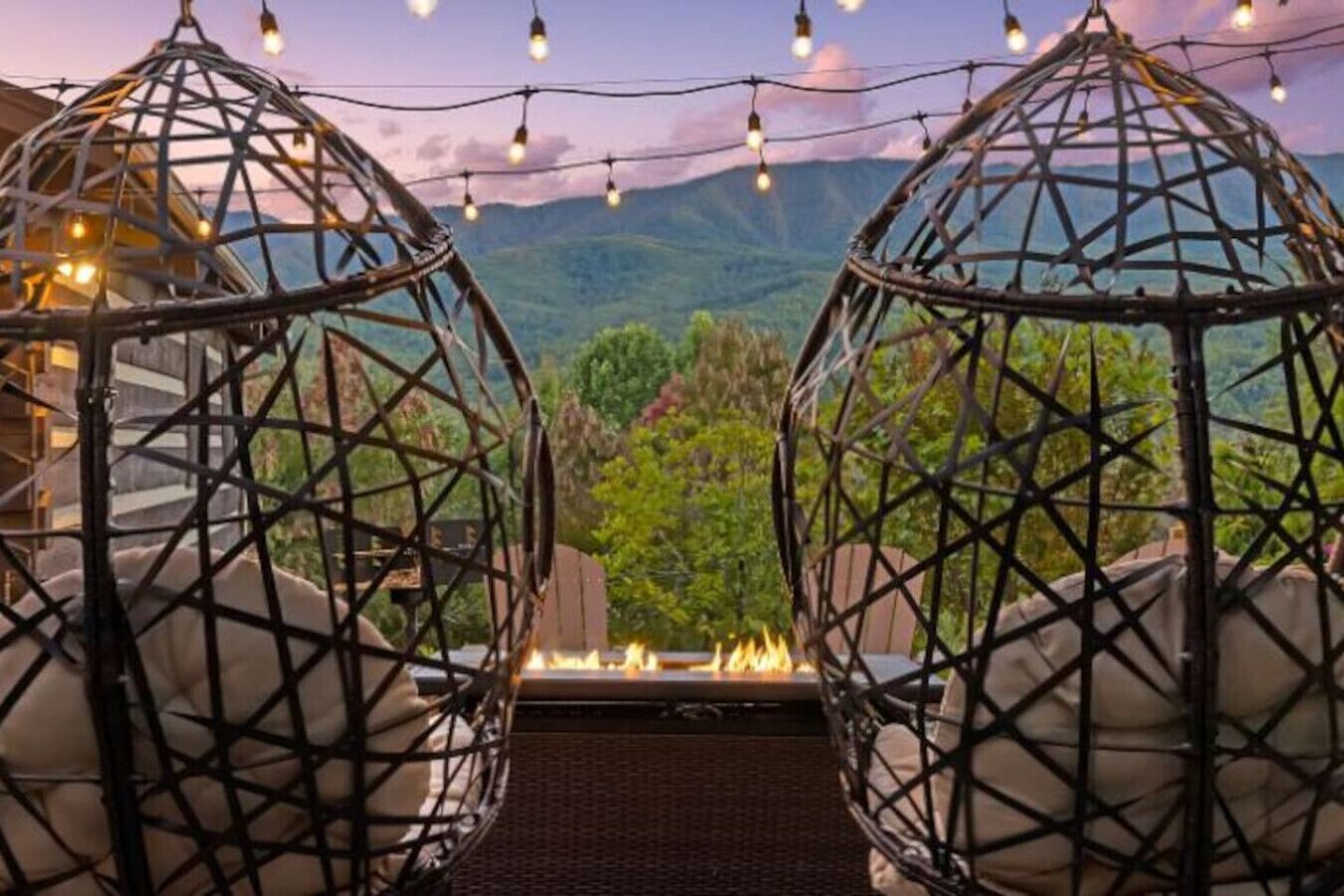 Two spherical wicker chairs with a fire feature in between, set against a backdrop of mountains and greenery.