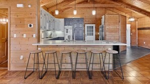 A spacious kitchen with a central island, bar stools, and wooden walls. - The Smoky Bear: View, Hot Tub, Pool & MORE! (Gatlinburg)