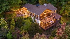 A large, multi-story log cabin with a deck and outdoor seating area, surrounded by dense forest. - The Smoky Bear: View, Hot Tub, Pool & MORE! (Gatlinburg)