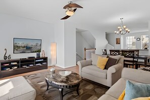 Ein modernes Wohnzimmer mit einer Couch, einem Couchtisch, einem Fernseher und einer Treppe, die in einen Essbereich führt.