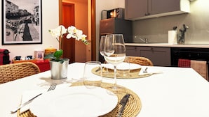 Een eetgedeelte met een tafel gedekt voor twee personen, een ingelijst beeld aan de muur en een keuken op de achtergrond.