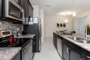 A modern kitchen with stainless steel appliances, a granite countertop, and a clean, minimalist design. - Villa Sanches 4BR w/ Pool – Storey Lake Resort (Kissimmee)