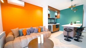Ein modernes Wohnzimmer mit einer Couch und einem Couchtisch, eine Küchenzeile mit einer Bar und einer Wand in Türkis.