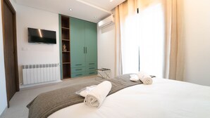 Ein modernes Schlafzimmer mit einem Bett, einem an der Wand montierten Fernseher, einem Kleiderschrank und einer Klimaanlage.