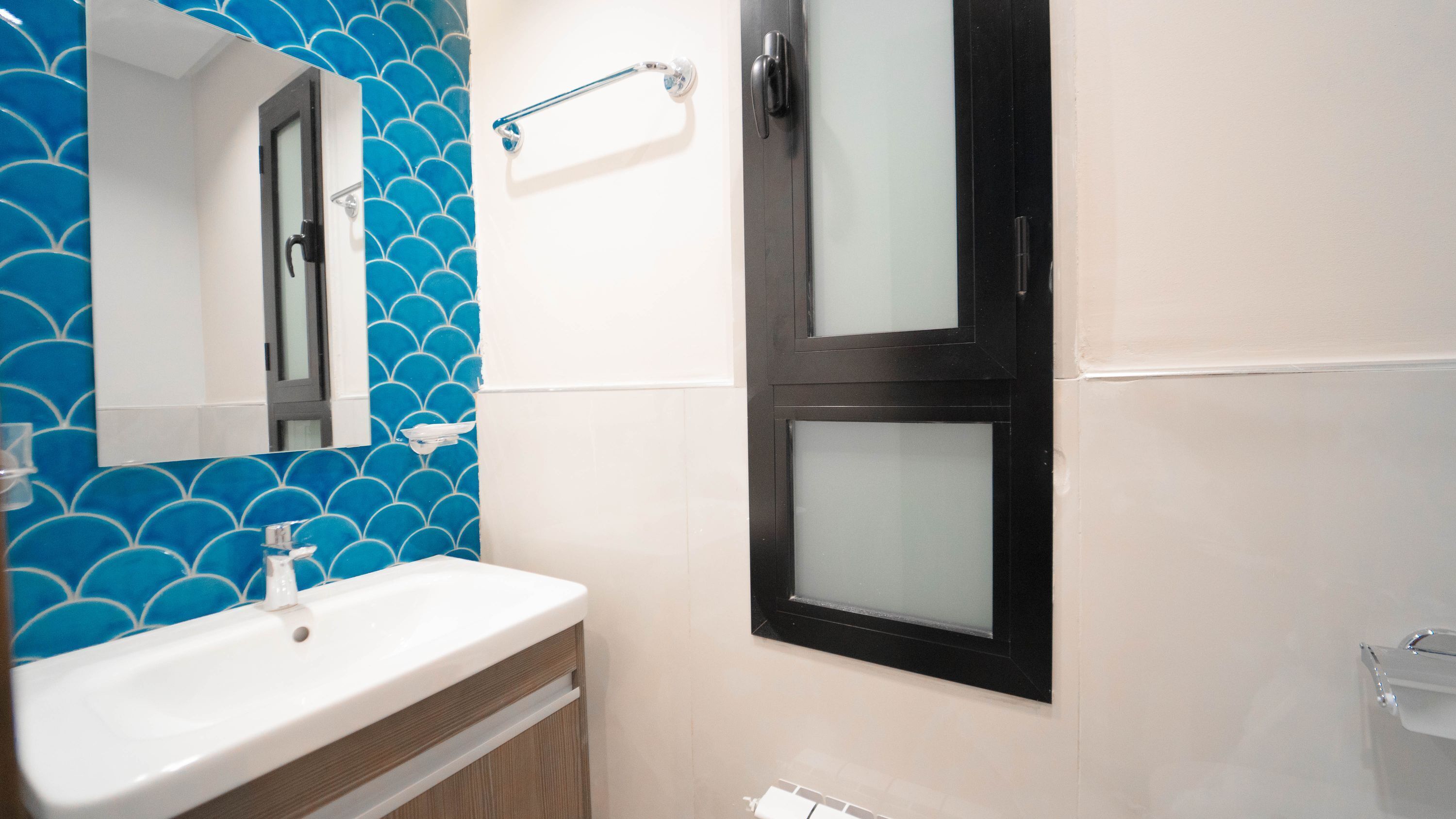 A bathroom with a white sink, blue tiled wall, and a black-framed mirror.