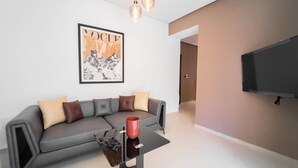 Un salon moderne avec un canapé gris, une tasse rouge posée sur une table en verre et une grande couverture de magazine encadrée accrochée au mur.