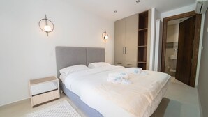 Une chambre à coucher avec un grand lit, des tables de chevet, une armoire et une salle de bain visible à travers une porte ouverte.