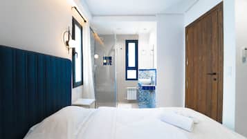 Une chambre moderne avec un grand lit, une porte en bois et une salle de bain équipée d’une douche et d’un lavabo.