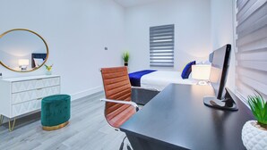 Ein modernes Schlafzimmer mit Bett, Schreibtisch, Stuhl, Spiegel und einer kleinen Pflanze.