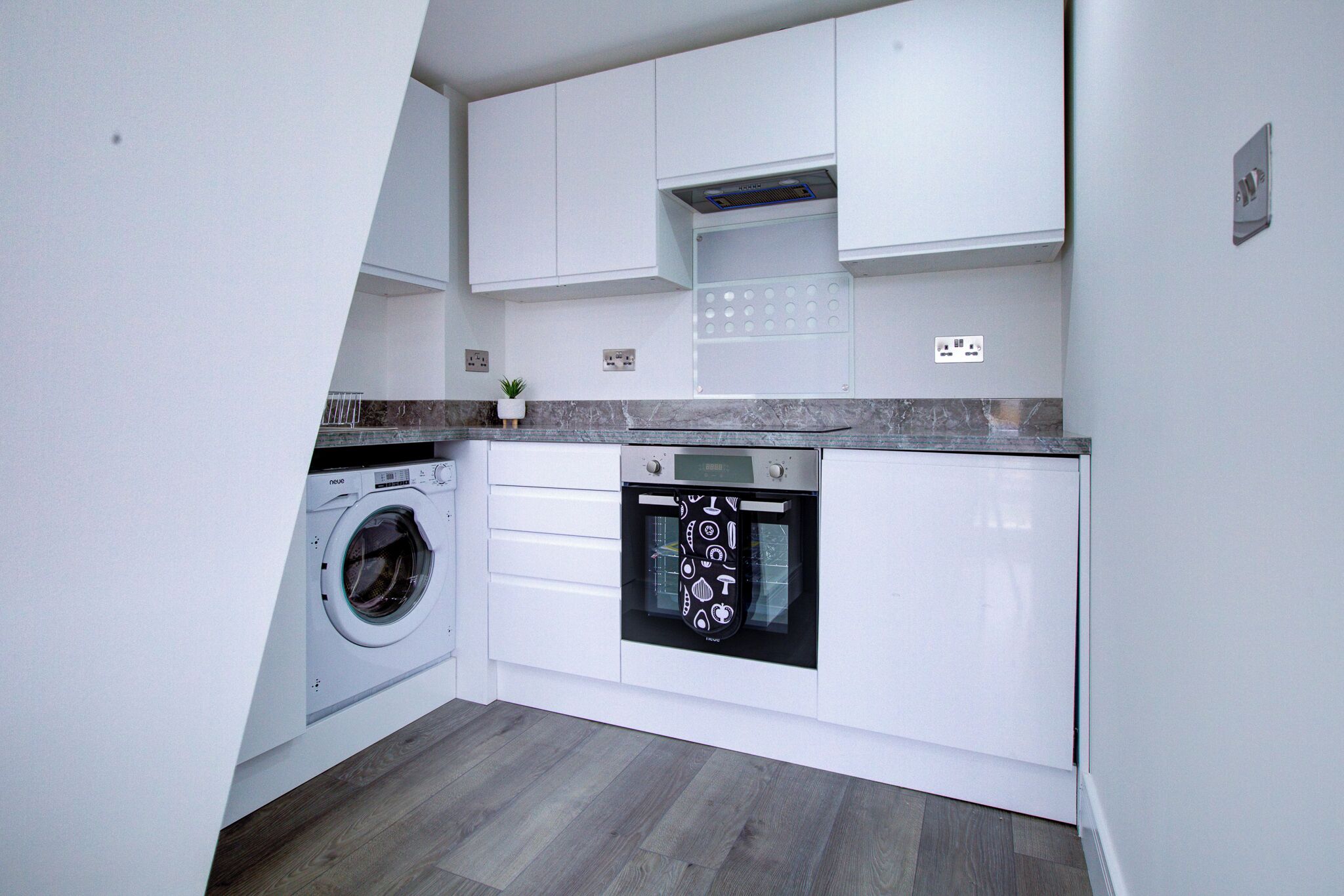 A compact kitchen with a washing machine, oven, and white cabinetry.