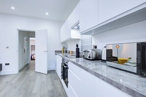 A modern kitchen with white cabinetry, a marble countertop, a built-in oven, and a toaster. - Hybrid Resi Wandsworth (London)