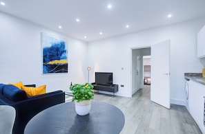 A modern living room with a sofa, a round table with a plant, a flat-screen TV, and a painting on the wall. - Hybrid Resi Wandsworth (London)