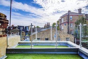 A rooftop with a small garden area, a brick building, and a clear sky. - Hybrid Resi Wandsworth (London)
