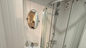 Pieni kylpyhuone, jossa on wc, pesuallas ja lasiseinällä varustettu suihku.