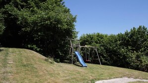 Un parque infantil con tobogán y columpios sobre una colina cubierta de césped.
