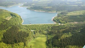 Vista aérea de un lago rodeado de bosques densos y un edificio pequeño cerca de la orilla.