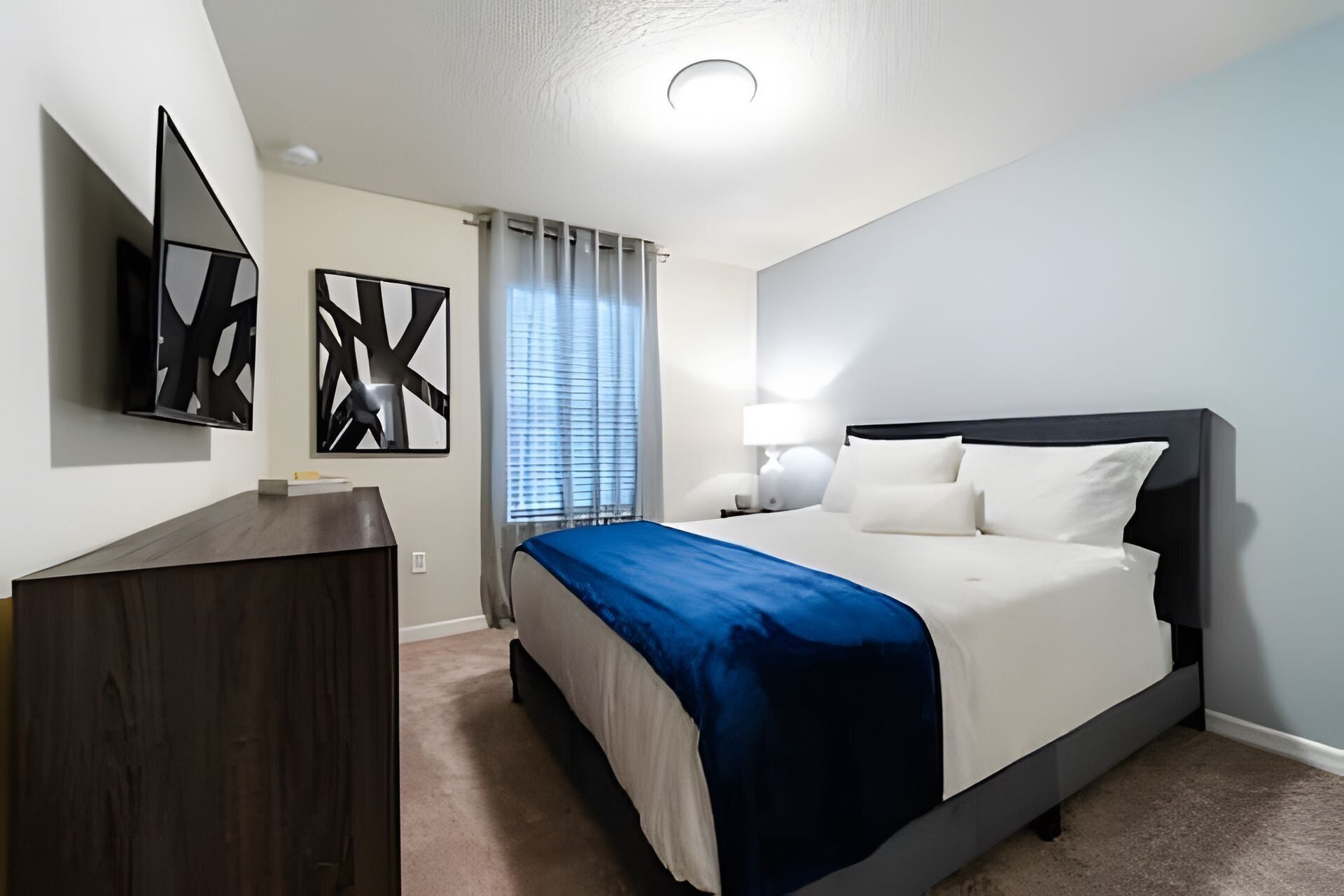 A modern hotel room with a bed, bedside table, lamp, and abstract artwork.