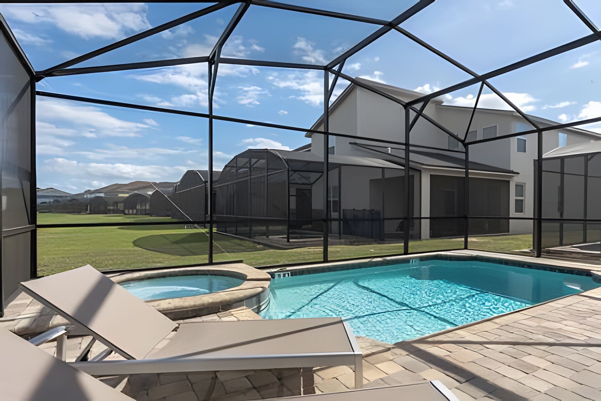 Ein Schwimmbad mit Glasveranda, eine Rasenfläche und ein Haus im Hintergrund.