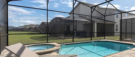 A swimming pool with a glass enclosure, a lawn, and a house in the background.