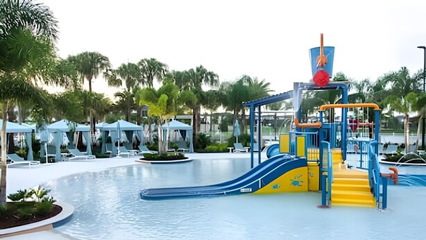 A water park with a blue and yellow slide, a pool, and lounge chairs. - Elegant 7BR Villa w/ Pool & Resort Access (Kissimmee)