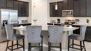A modern kitchen with dark cabinets, stainless steel appliances, and a central island with bar stools. - Elegant 7BR Villa w/ Pool & Resort Access (Kissimmee)