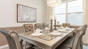 A dining room with a glass-top table, cushioned chairs, and a chandelier. - Elegant 7BR Villa w/ Pool & Resort Access (Kissimmee)