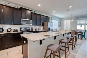 A modern kitchen with dark cabinets, stainless steel appliances, and a large island with bar stools. - Modern 6BR Villa w/ Pool & Resort Access (Kissimmee)