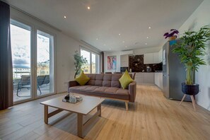 Un salon moderne avec un canapé, une table basse et une vue sur la ville grâce à de grandes fenêtres.