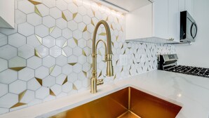 A kitchen with a white countertop, a copper sink, and a backsplash with hexagonal tiles. - Spacious 2BR Apartment, 10 min to Time Square! (Weehawken Township)