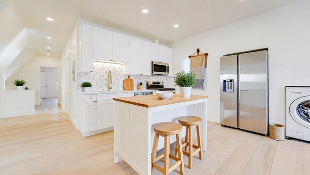 A modern kitchen with white cabinetry, a central island with stools, a stainless steel refrigerator, and a washing machine. - Spacious 2BR Apartment, 10 min to Time Square! (Weehawken Township)