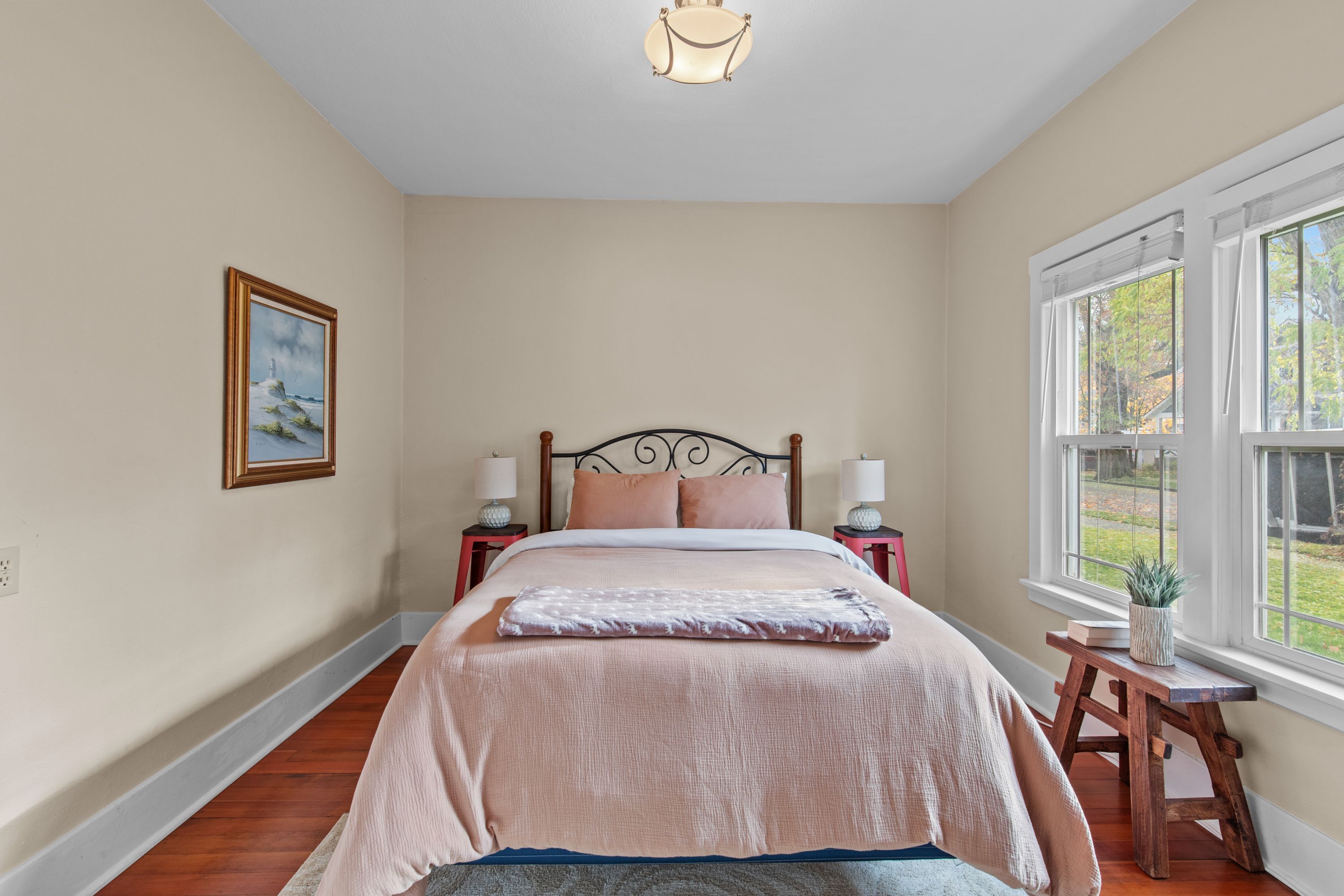 A bedroom with a bed, bedside tables, a window with a view, and a painting on the wall.