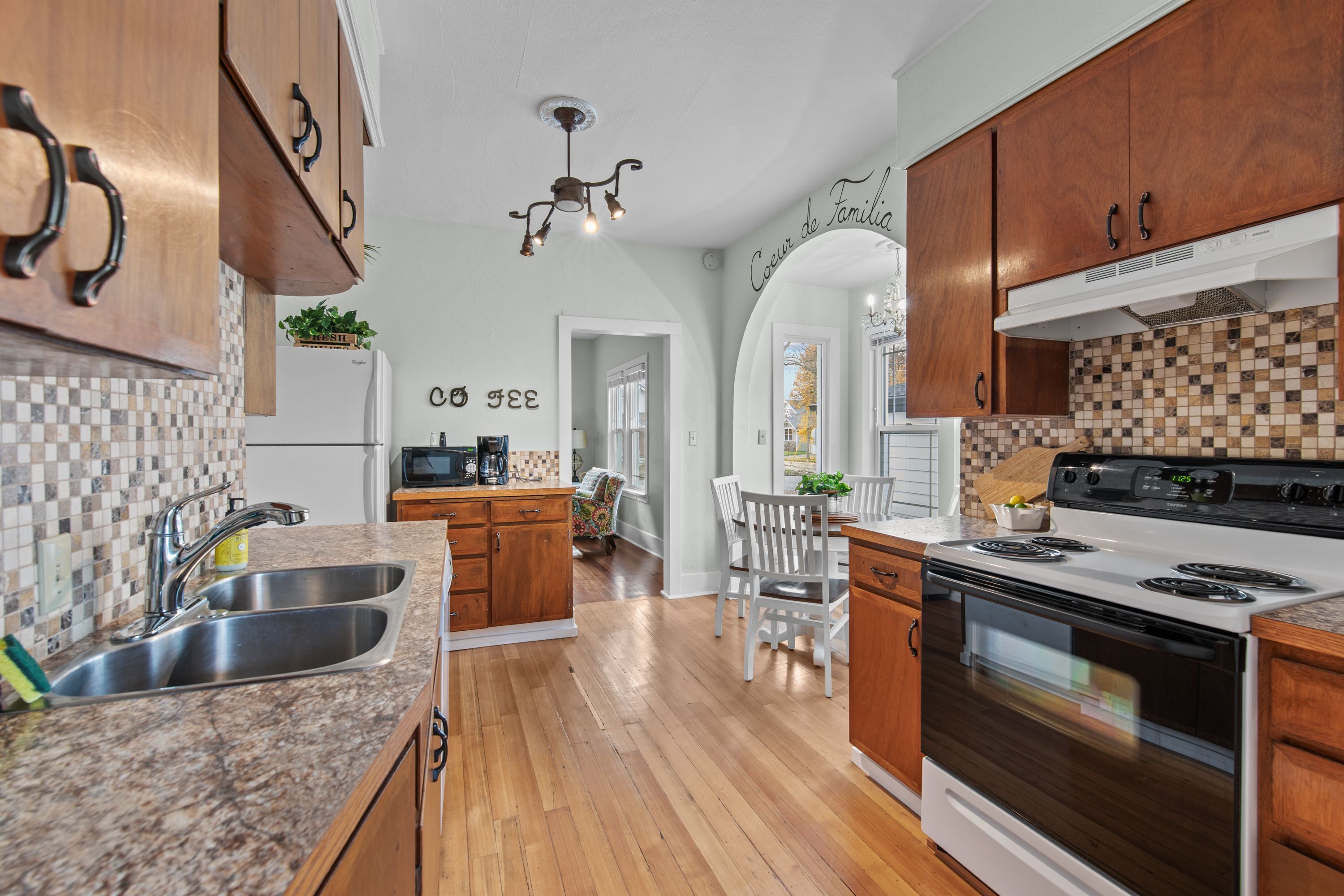 A kitchen with wooden cabinets, a stainless steel sink, a white stove, and a tiled backsplash.