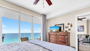 A bedroom with a large bed, a dresser, a television, and a view of the ocean. - Emerald Isle 1406 (Panama City Beach)