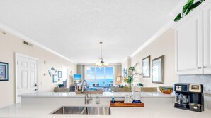 A modern kitchen with white cabinetry, a stainless steel sink, and a coffee maker. - Emerald Isle 1406 (Panama City Beach)